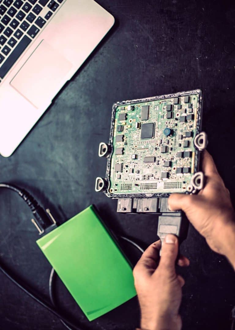technician holding an opened engine ecu next to a bench flashing tool and laptop